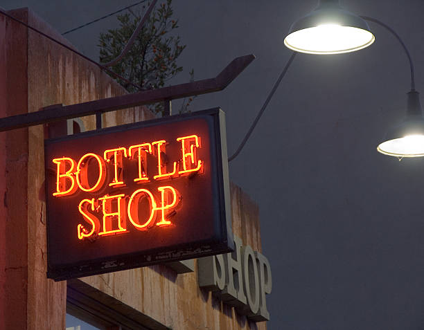 Neon bottle shop sign on pub wall at evening